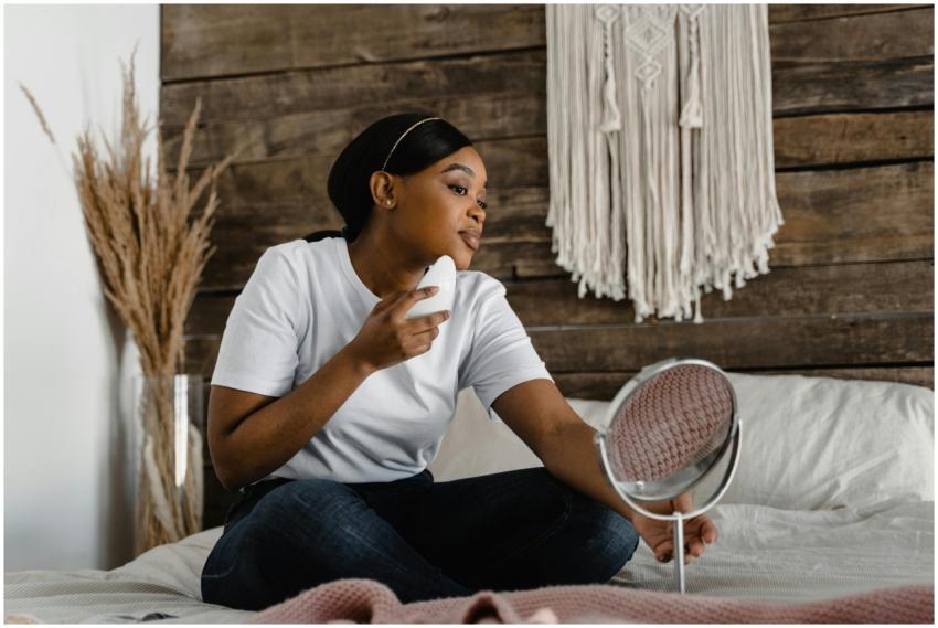 A woman sitting on a bed using a mirror for a skin
