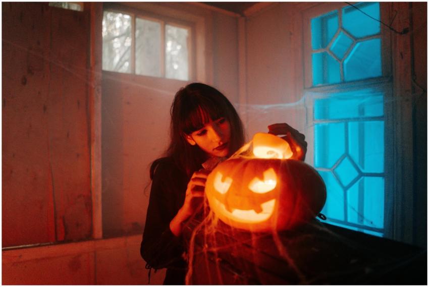 A woman carves a glowing jack-o'-lantern indoors a
