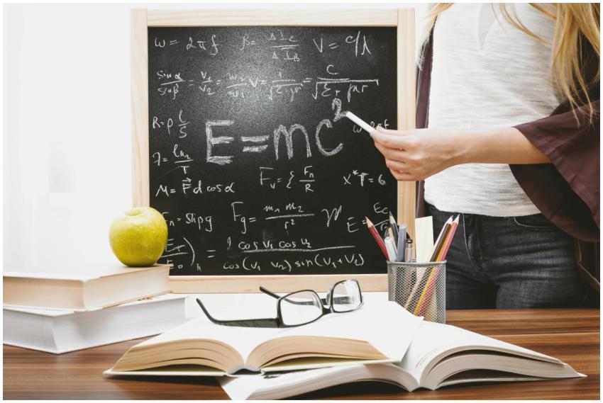 Woman writing physics equations on a blackboard wi