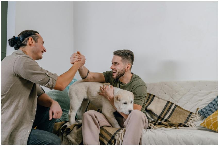 Two men sitting on a couch with a dog, sharing a f