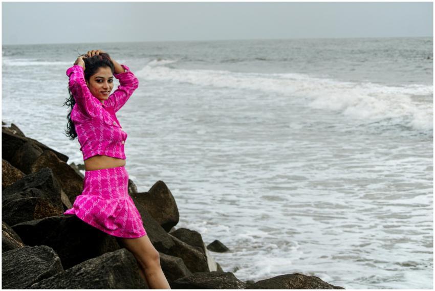 Woman in pink outfit posing on rocks by the ocean,