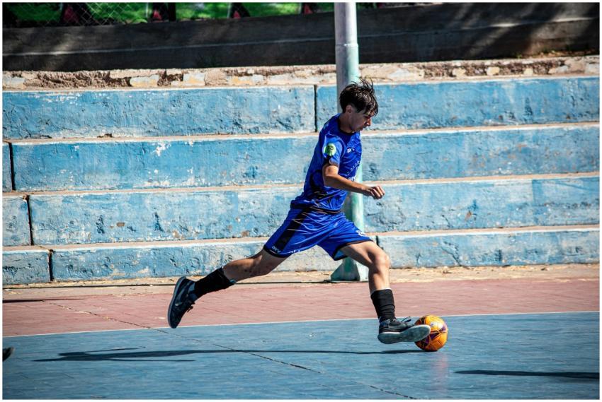 Teenage boy in blue jersey playing soccer on an ou