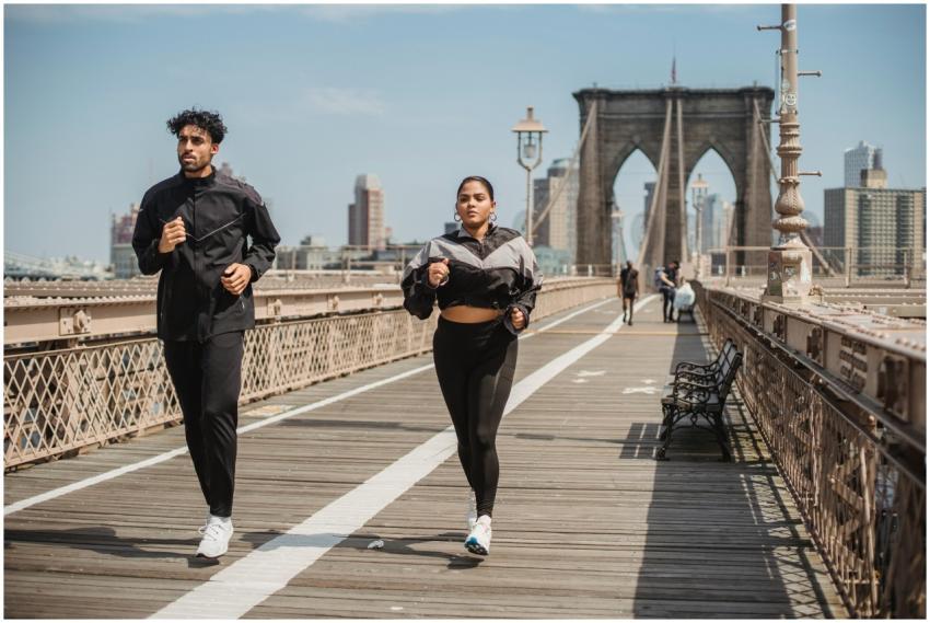 Two adults jogging on Brooklyn Bridge with city sk