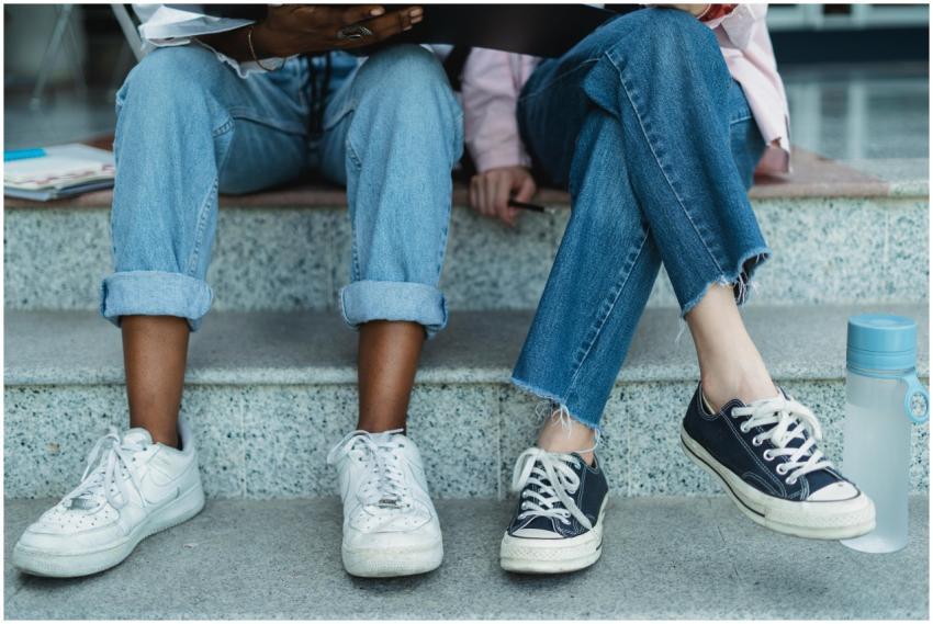 Two friends in jeans and sneakers sitting on an ou