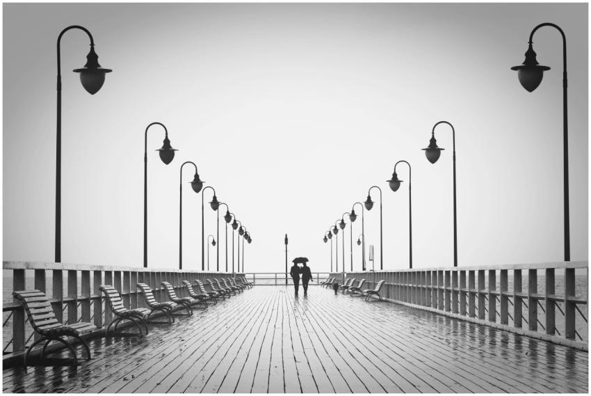 A couple holding umbrellas walks on a rainy boardw