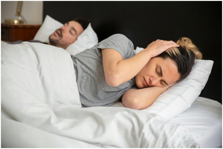 A woman looks frustrated in bed as her partner sno