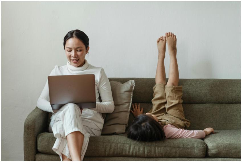 A mother working on a laptop while her daughter li