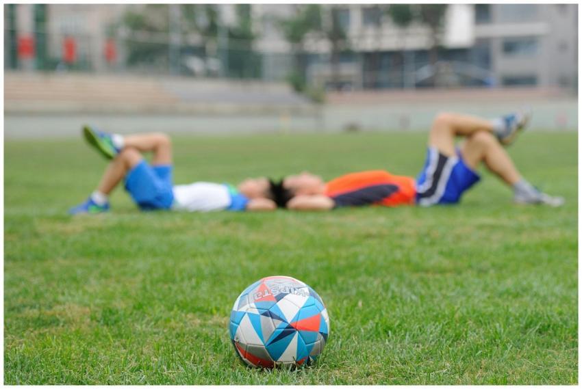 Two teenagers lying on grass near a soccer ball, e