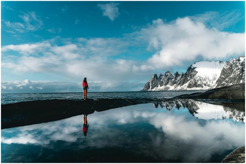 A person stands by a scenic snowy coastline reflec
