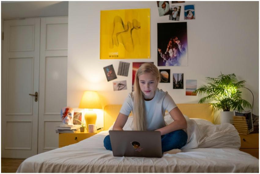 Teen girl using a laptop in her cozy bedroom lit w