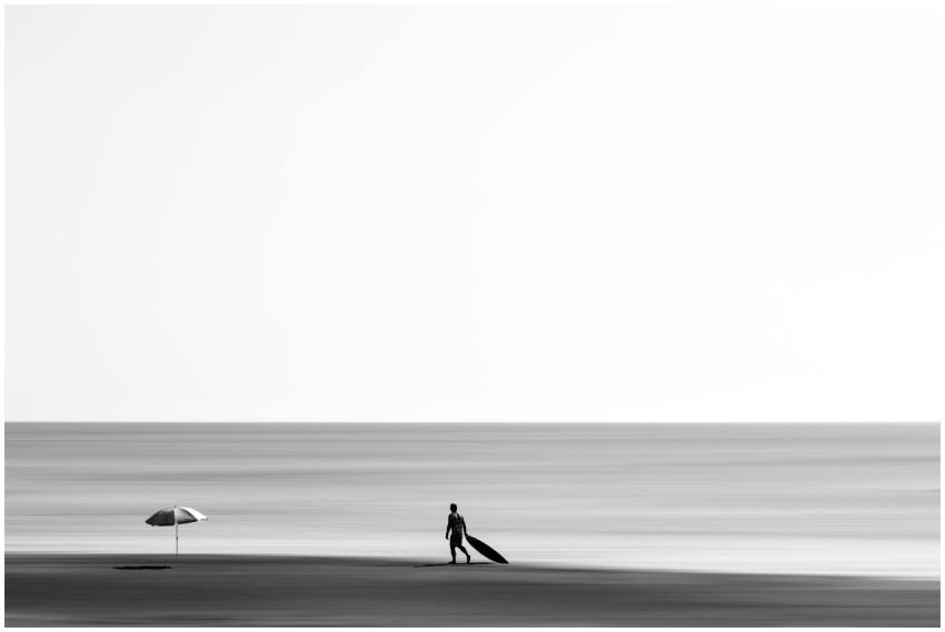 Minimalist black and white photo of a surfer walki