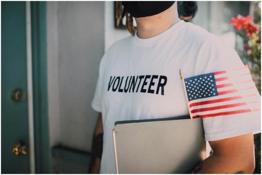 Volunteer wearing a mask holds a notebook and Amer
