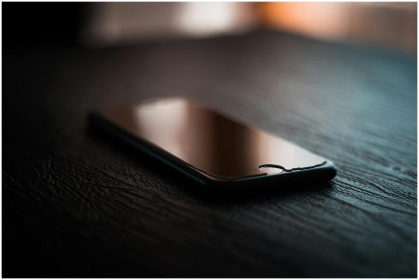 A smartphone lies on a dimly lit wooden table show