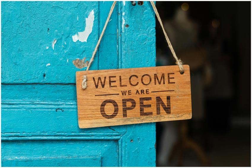 A rustic wooden 'Welcome We Are Open' sign hanging
