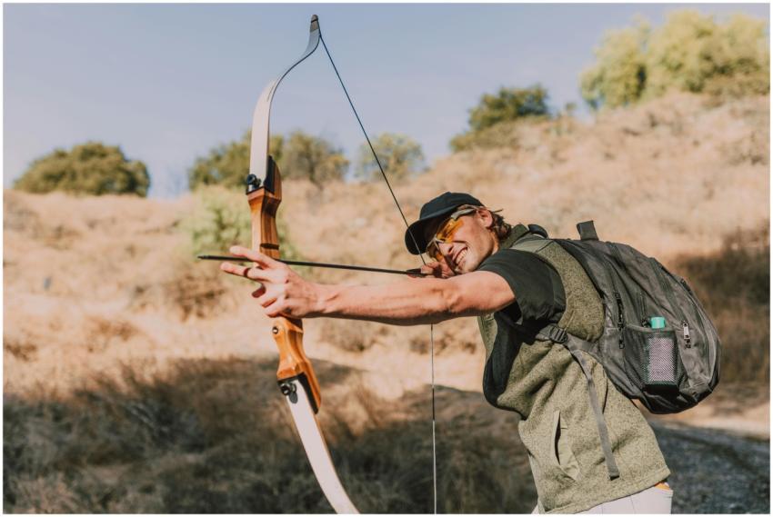 A man skillfully aiming a recurve bow outdoors, sh