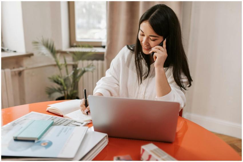 Young woman multitasking with laptop and phone in