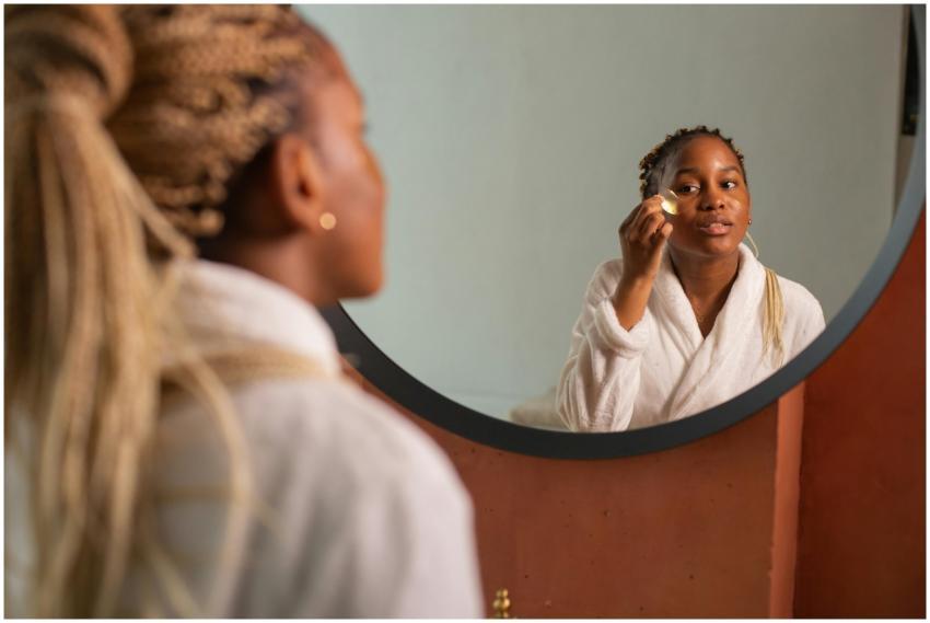 Young woman in robe applying skincare with mirror