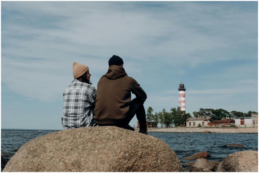 A couple sits on a rock by the sea, gazing at a li