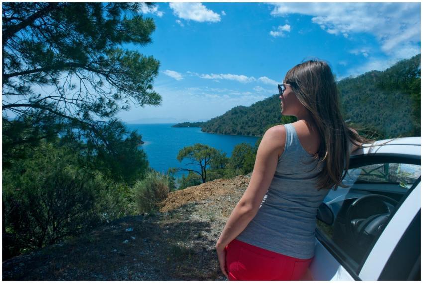 Woman leaning on car, gazing over scenic coastal v