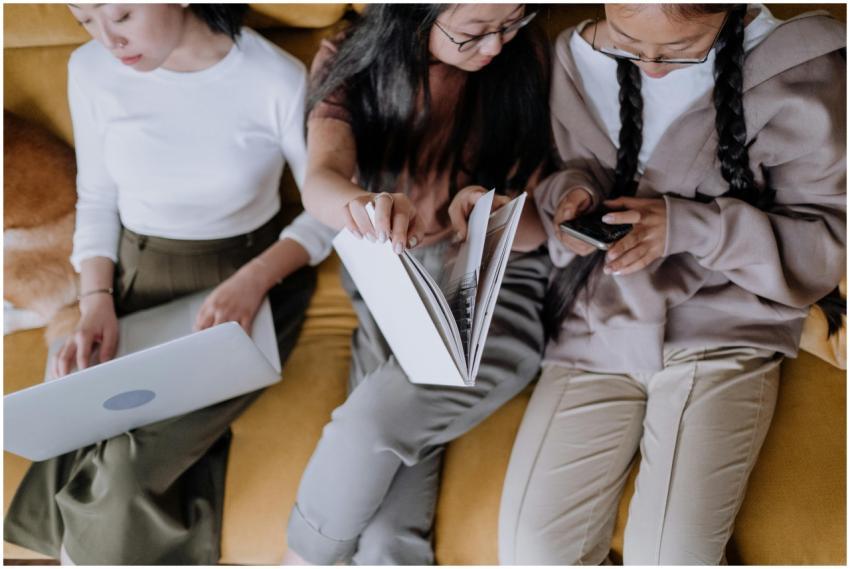 Three women relaxing on a sofa, using gadgets and