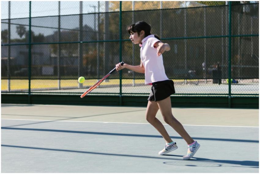 A young girl energetically playing tennis on an ou