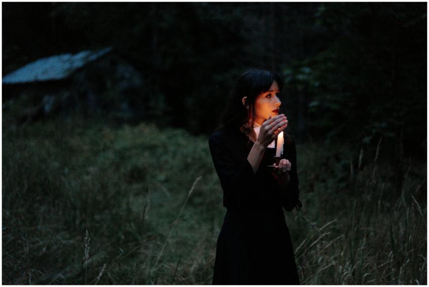 A woman holding a candle in a dark forest evokes a
