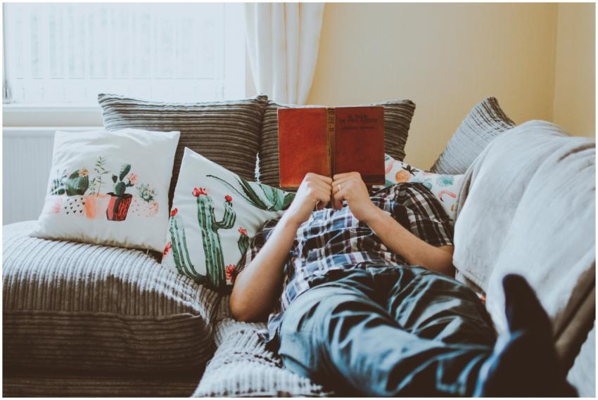 Relaxing at home, lying on a sofa with a book and