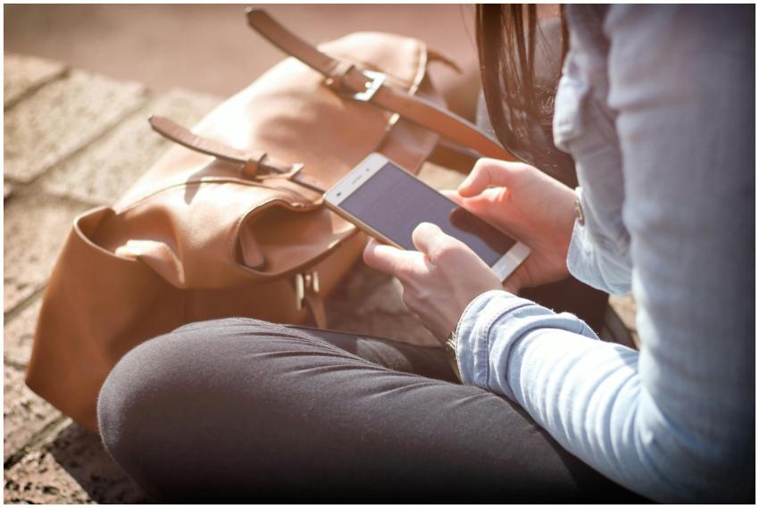 Woman sitting with smartphone and brown bag in sun