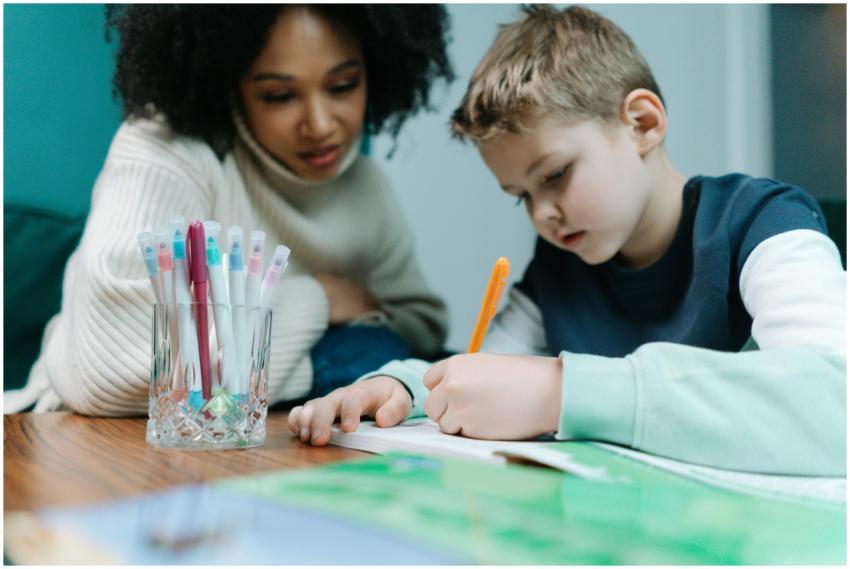 A young child writes while being supported by a te