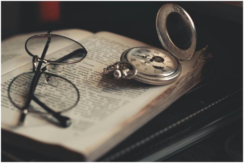 A vintage pocket watch and glasses lying on an ope