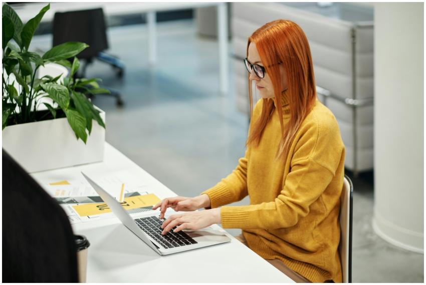 A woman in a mustard sweater working on her laptop