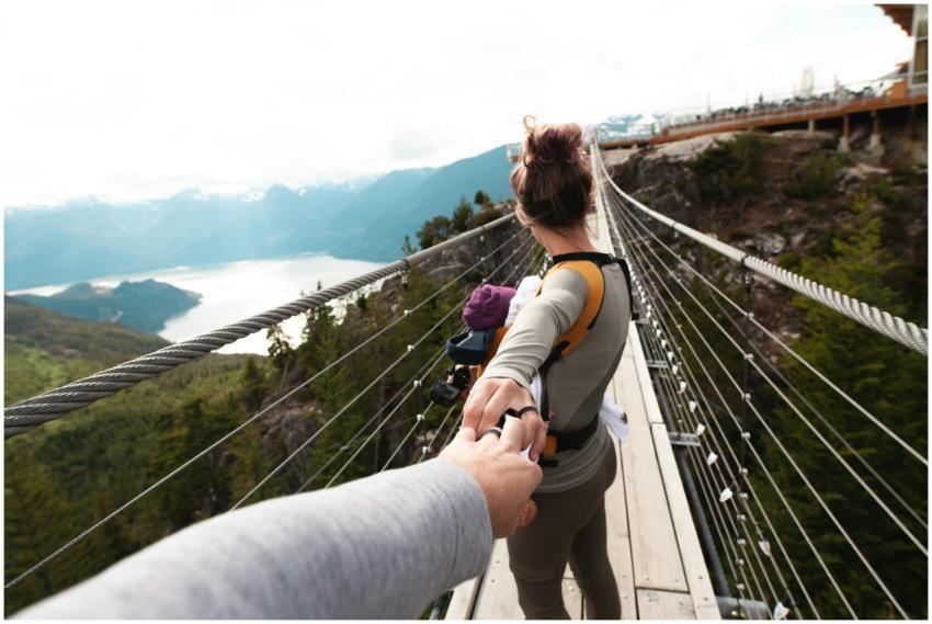 A woman with a baby crosses a scenic hanging bridg