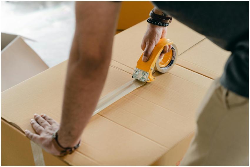 Man using packing tape to seal a cardboard box ind