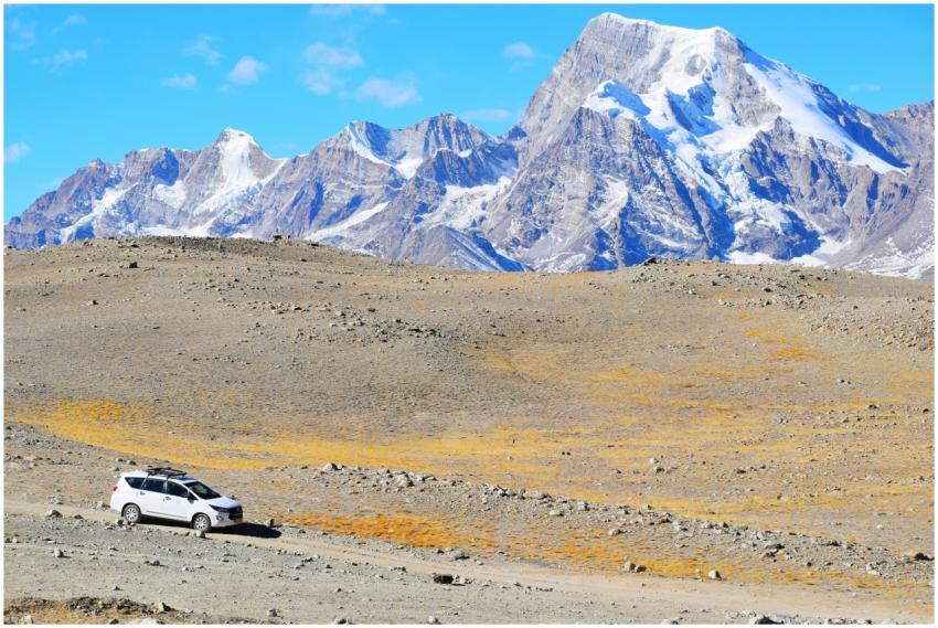 A vehicle traverses rugged terrain below snow-capp