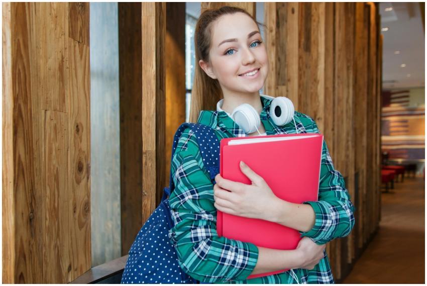 Smiling student holding book and wearing headphone
