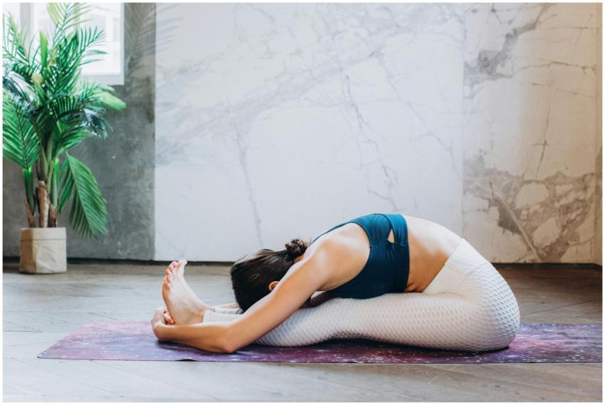 Woman performing a seated forward bend yoga pose o