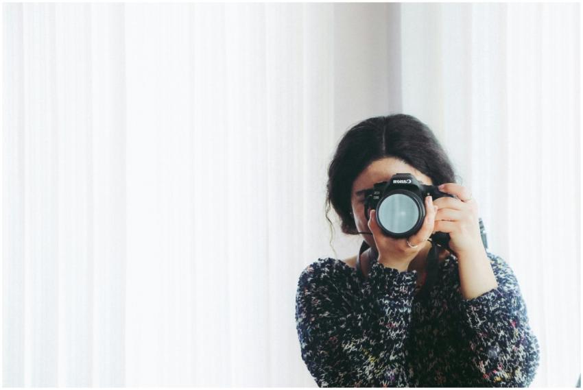 A young woman holding a camera indoors, capturing