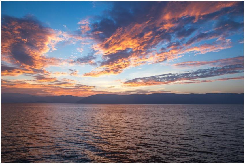 A vibrant sunset with dramatic clouds reflects ove