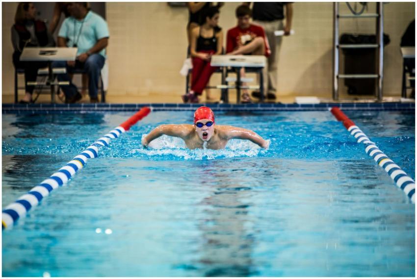 A young swimmer in a red cap competes in a butterf