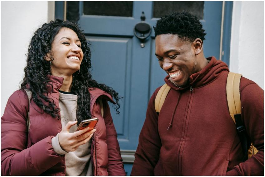 Two young adults smile and chat in front of a blue