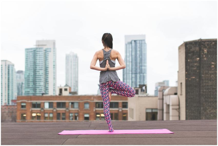 A woman performs yoga on a rooftop with a city sky