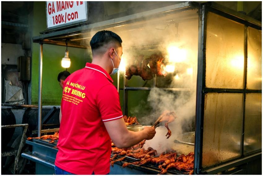 Street vendor grilling chicken with steam rising,