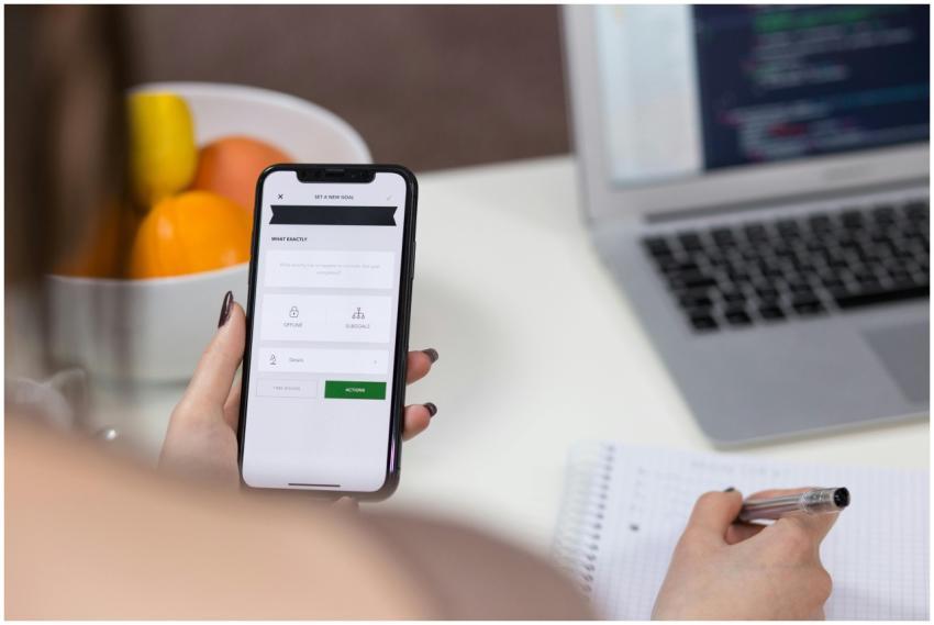 A person using a smartphone and taking notes on a