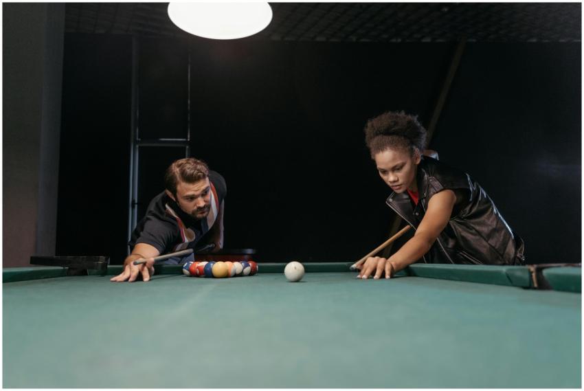 Two people focusing on a game of pool, aiming to m