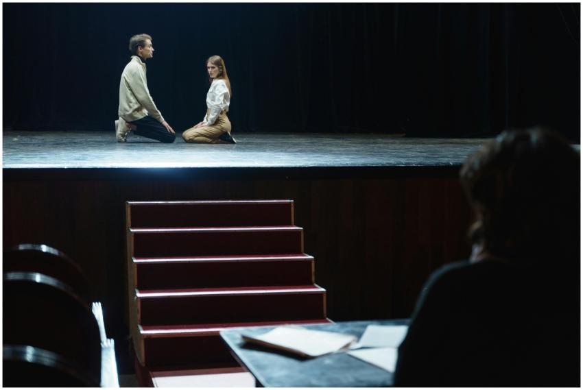 Actors in a dramatic rehearsal on stage, under dim