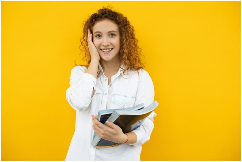 Happy young woman holding textbooks against a vibr