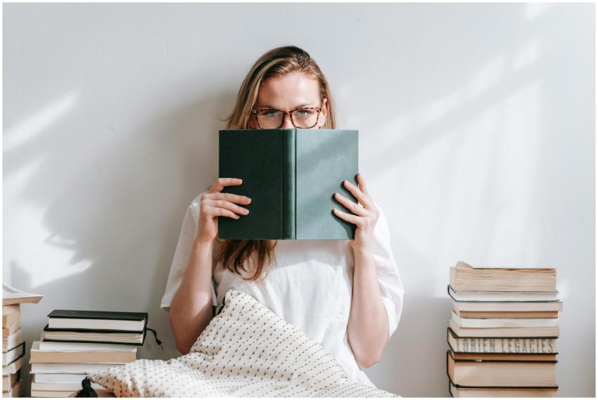 Young woman with eyeglasses reading book indoors,