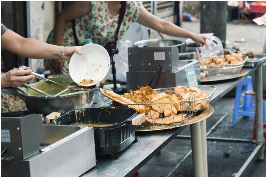 Street food stall with hands preparing fried dishe