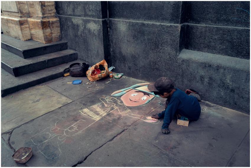 A young boy creates vibrant pavement art on a city