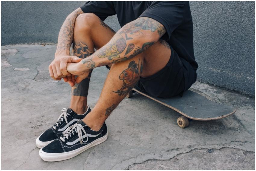 A tattooed man sits casually on a skateboard again